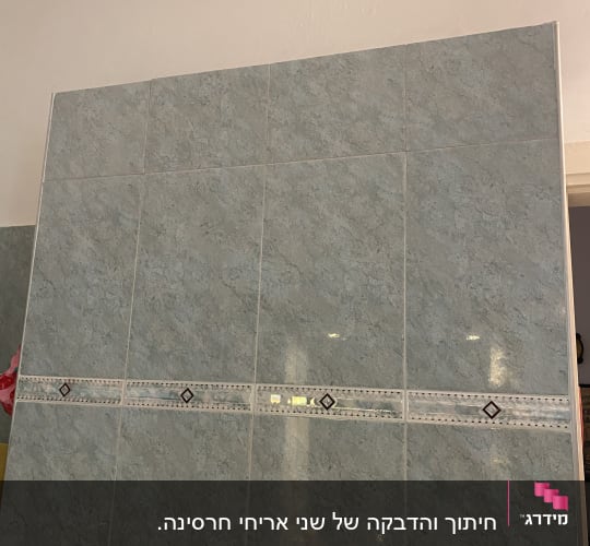 חיפוי קיר אריחים בגוון תכלת-אפור עם פס דקורטיבי ורובה נקייה